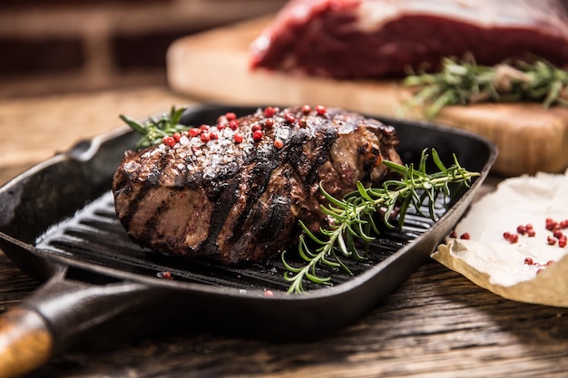 Gegrilltes Rindersteak in Grillpfanne mit Kräuterrosmarin auf Holztisch.