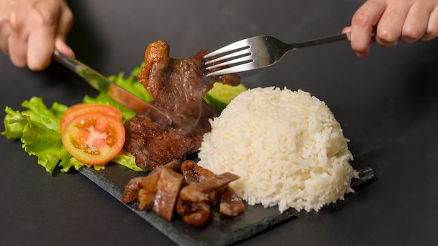Gegrilltes Rindfleisch mit Reis auf Platte über schwarzem Hintergrundstudio