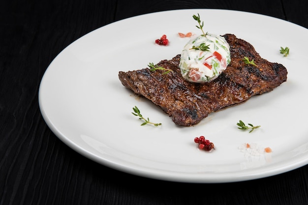 Gegrilltes Rockbeefsteak auf einem Teller mit weißer Gemüsesauce, dekoriert mit Kräutern und Beeren...