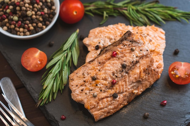 Gegrilltes rotes Fischfleisch-Lachssteak mit Tomaten-Rosmarin und Gewürzen auf schwarzem Steinhintergrund