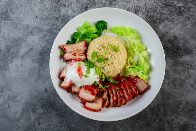 Gegrilltes rotes schweinefleisch und knuspriges schweinefleisch in roter sauce, serviert mit reis und gemüse auf weissem teller,