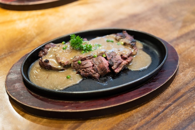 Gegrilltes, saftiges Steak Medium Rare Beef mit Kräutern und Gewürzen in einer heißen Pfanne, garniert mit schwarzer Pfeffersoße