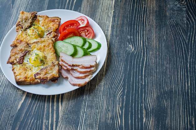 Gegrilltes Sandwich mit Ei, Gemüse und Speck auf einem dunklen Holz