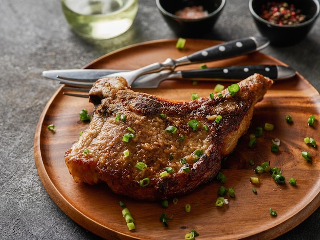 Gegrilltes Schweinekotelett auf grauer Platte, bestreut mit Frühlingszwiebeln auf dem grauen Hintergrund der Holzplatte