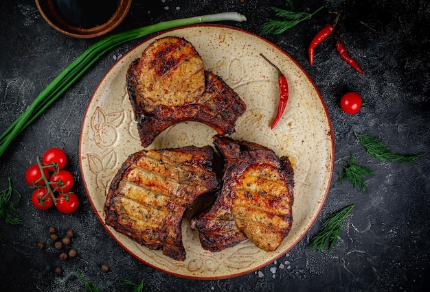 Gegrilltes Schweinelende-Schweinesteak am Knochen auf einem dunklen Steintisch mit Gemüsecreme und Tomatensoße, serviert auf einem Tonteller Fast-Food-Restaurant-Lieferservice