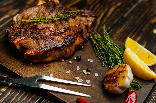 Gegrilltes Steak auf Schneidebrett mit Zitrone, rotem Pfeffer, Knoblauch und Gewürzen auf dunklem Rustikal