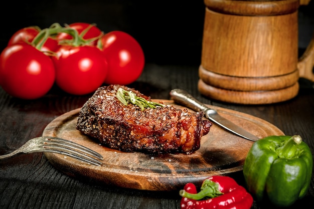 Gegrilltes Steak gewürzt mit Gewürzen und frischen Kräutern serviert auf einem Holzbrett mit Holzkrug Bier ...