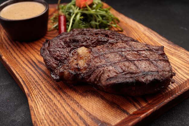 Gegrilltes Steak mit Sauce und Kräutern auf einem Holzbrett