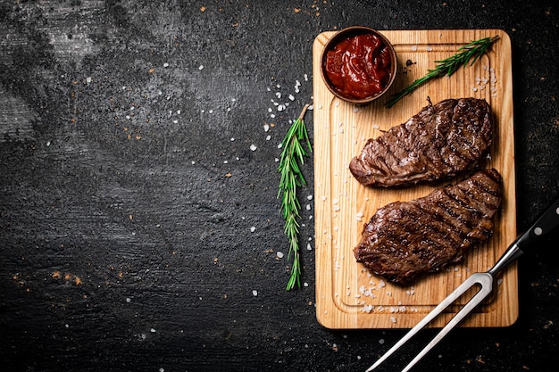 Gegrilltes Steak mit Tomatensauce und Rosmarin auf einem Schneidebrett