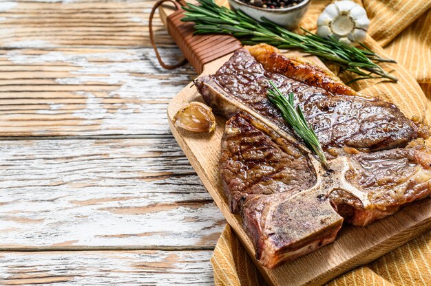 Gegrilltes T-Bone-Steak auf einem Schneidebrett. Gekochtes Rindfleisch mit Knochen. Weißer Holzraum. Draufsicht. Speicherplatz kopieren