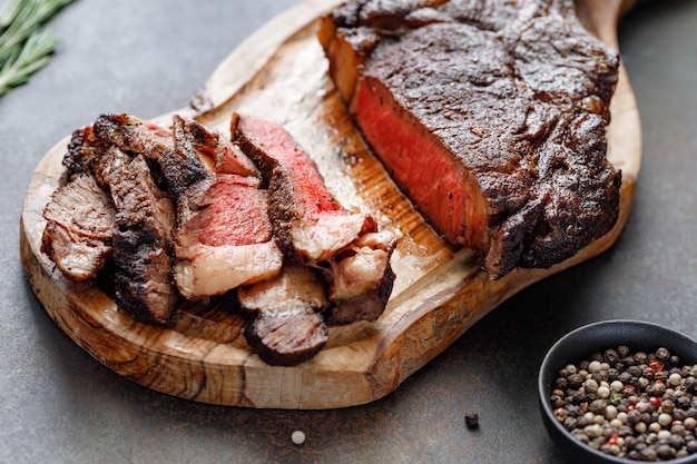 Gegrilltes trocken gereiftes Rindersteak aus Marmor Tomahawk auf schwarzem Holzbrett mit Gewürzen