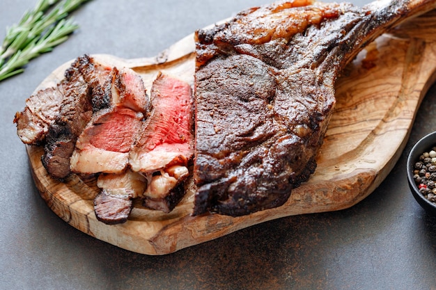 Gegrilltes trocken gereiftes Rindersteak aus Marmor Tomahawk auf schwarzem Holzbrett mit Gewürzen