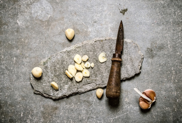 Gehackter Knoblauch und altes Messer auf einem Steinständer. Auf einem steinernen Hintergrund.