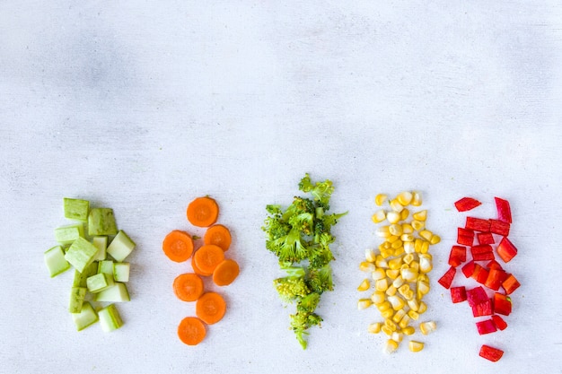 Gehacktes Gemüse auf dem weißen Tisch, Karotten, Brokkoli, Mais und Paprika