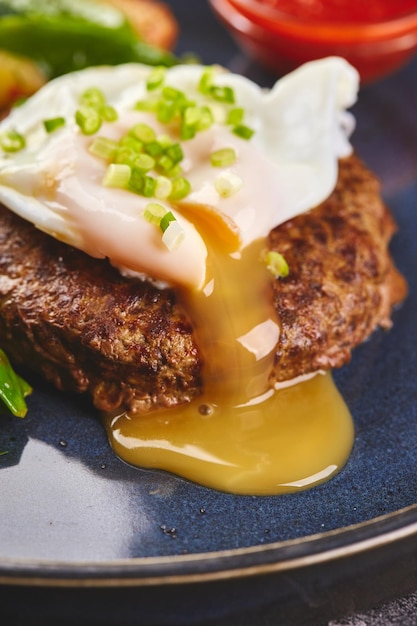 Gehacktes Rindersteak mit pochiertem Ei und Gemüsegarnitur mit Tomatensauce auf dem Teller