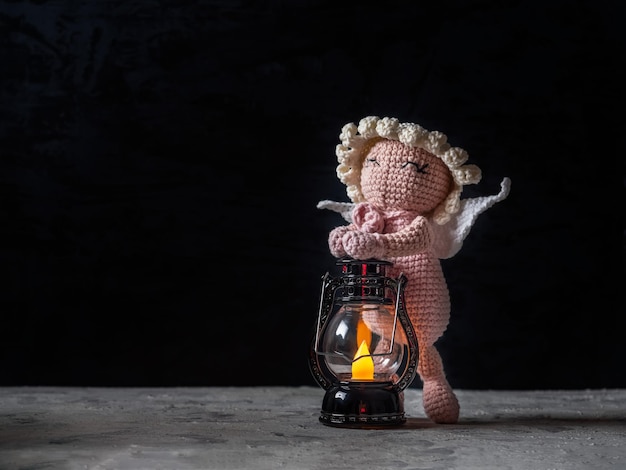 Gehäkelter rosa Babyengel, der eine brennende Lampe auf einem dunklen Hintergrund hält