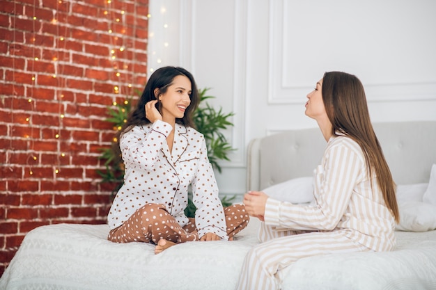 Geheimnisse teilen. Zwei junge Mädchen im Pyjama sitzen auf einem Bett und reden