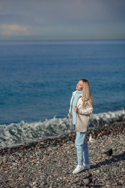 Gehen Sie in der kalten Jahreszeit am Meer entlang, eine Frau in warmer Kleidung blickt über den Horizont auf das Meer