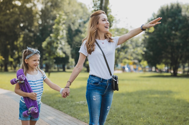 Gehen Sie mit der Tochter. Stilvolle Mutter, die dunkle Umhängetasche trägt, die einen unvergesslichen Spaziergang mit Tochter hat