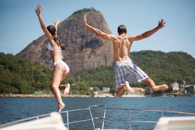 Gehen Sie wild in diesem Urlaub Rückansicht eines jungen Paares, das von einer Yacht ins Meer springt