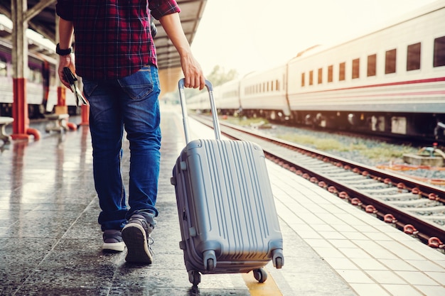 Gehendes Draggepäck des jungen touristischen Mannes. Die andere Hand hält die Karte und geht zum Zug