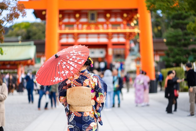 Geishas-Mädchen, das japanischen Kimono unter rotem hölzernem Tori Gate trägt
