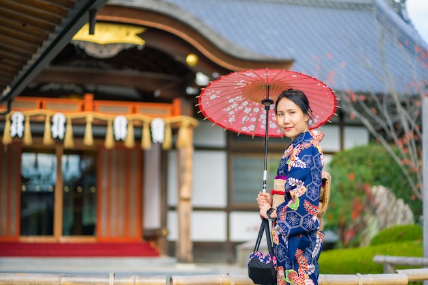 Geishas Mädchen, das japanischen Kimono unter rotem hölzernen Tori-Tor am Fushimi Inari-Schrein in Kyoto trägt,