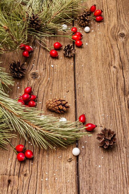 Geist-Weihnachten auf Holztisch. Frische Heckenrosenbeeren, Ballsüßigkeiten, Tannenzweige und Zapfen, Kunstschnee. Naturdekorationen, hölzerne Bretter der Weinlese