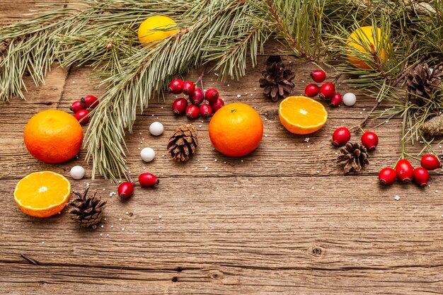 Geist-Weihnachten auf Holztisch. Frische Mandarinen, Heckenrose, Bonbons, Tannenzweige und Zapfen, Kunstschnee