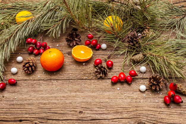 Geist-Weihnachten auf Holztisch. Frische Mandarinen, Heckenrose, Bonbons, Tannenzweige und Zapfen, Kunstschnee