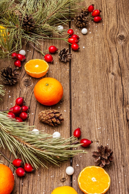 Geist-Weihnachten auf Holztisch. Frische Mandarinen, Heckenrose, Bonbons, Tannenzweige und Zapfen, Kunstschnee