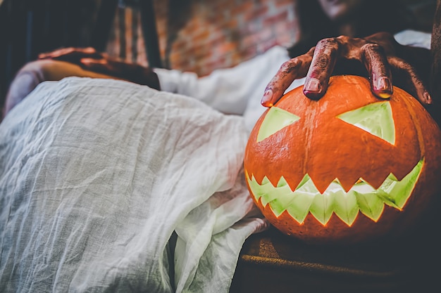 Geistermädchen im Blut mit dem weißen Kleid, das den Halloween-Kürbis hält