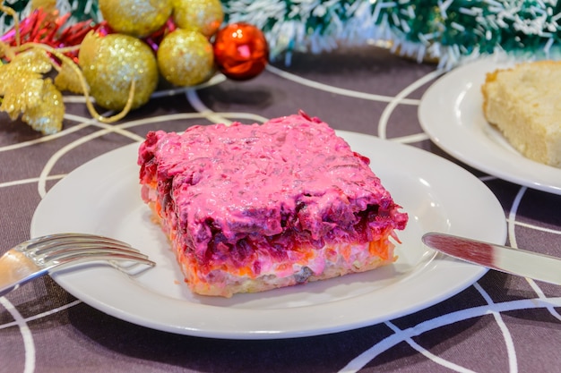 Gekleideter Hering oder Hering unter einem Pelzmantel. Symbol des neuen Jahres. Traditionelle russische Küche. Weihnachtsschmuck im Hintergrund. Neujahrskonzept.