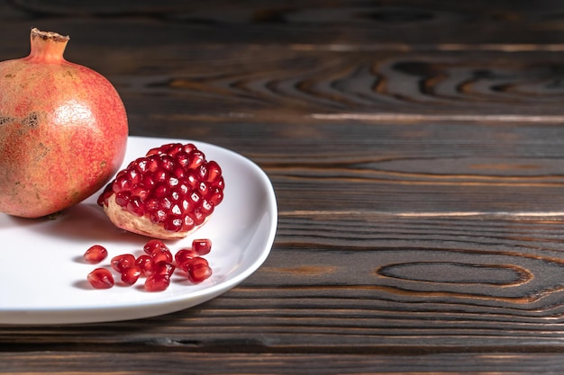 Geknackte reife Granatapfel- und Granatsamen in weißer Platte auf dunklem Holzschreibtisch mit Platz für Text