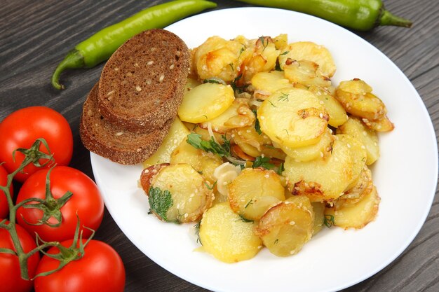 Gekochte Bratkartoffeln mit Kräutern und Gemüse in einem Teller auf einem Holztisch
