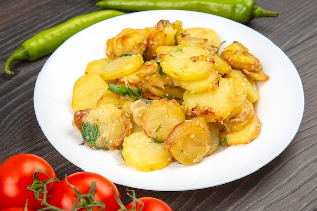Gekochte Bratkartoffeln mit Kräutern und Gemüse in einem weißen Teller auf einem Holztisch