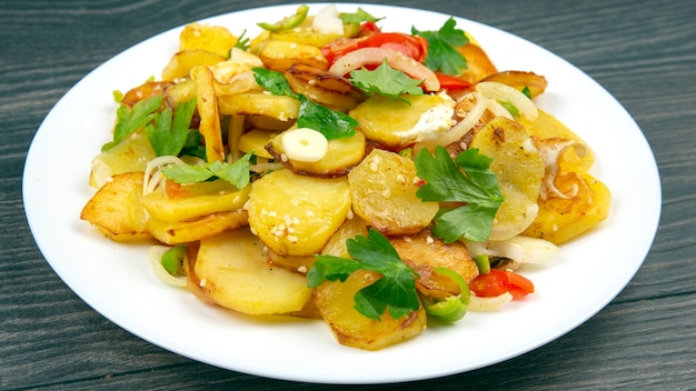 Gekochte Bratkartoffeln mit Kräutern und Gemüse in einem weißen Teller auf einem Holztisch