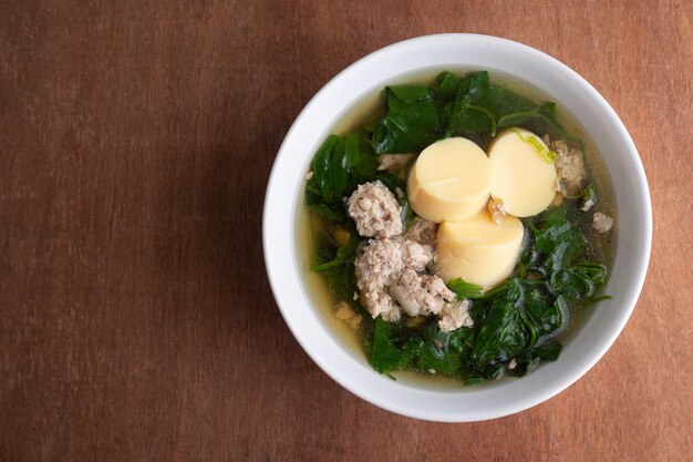 Gekochte gehackte Schweinefleisch- und Tofusuppe mit Kürbis in weißer Schüssel auf Holztisch, thailändisches Essen, gesundes Essen.