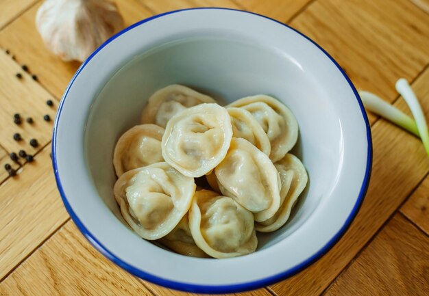 Gekochte hausgemachte russische Pelmeni-Knödel Ravioli mit Fleisch auf grauem Teller mit frischem Petersiliepfeffer hölzerner rustikaler Hintergrund Top-View