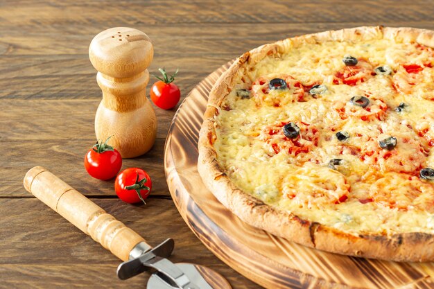 Gekochte heiße Pizzatorte mit Peperoni, Tomaten, schwarzen Oliven und Mozzarella auf Holzbrett.