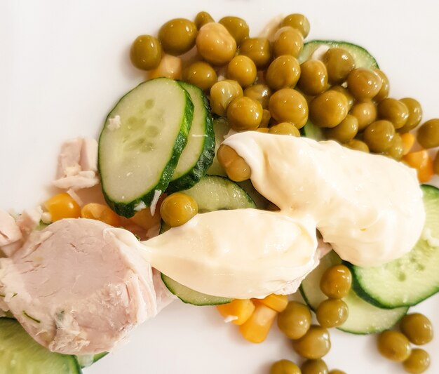 Gekochte Hühnerbrust mit grünen gekochten Erbsen, Gurke und Sauce auf einem weißen Teller. Gesunde ausgewogene Ernährung, das Konzept einer Diät