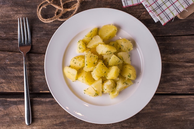 Gekochte Kartoffeln mit Dill auf weißer Platte auf rustikaler hölzerner Tabelle