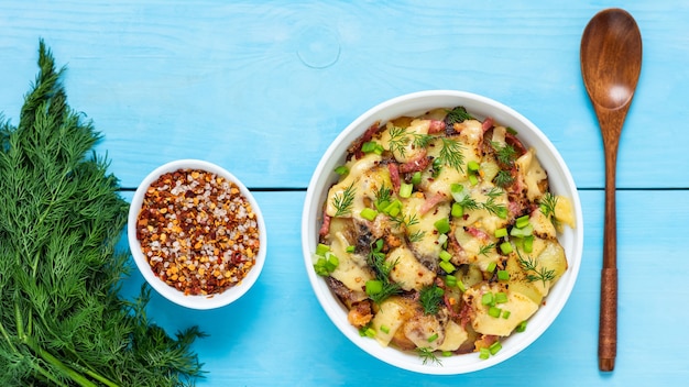 Gekochte Tartiflette mit Speck und Kräutern auf einem blauen Holztisch. Draufsicht.