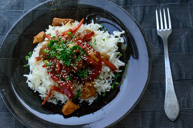 Gekochter Aufgang mit Hühnerstücken und Paprika, bedeckt mit Sesam und Gemüse.