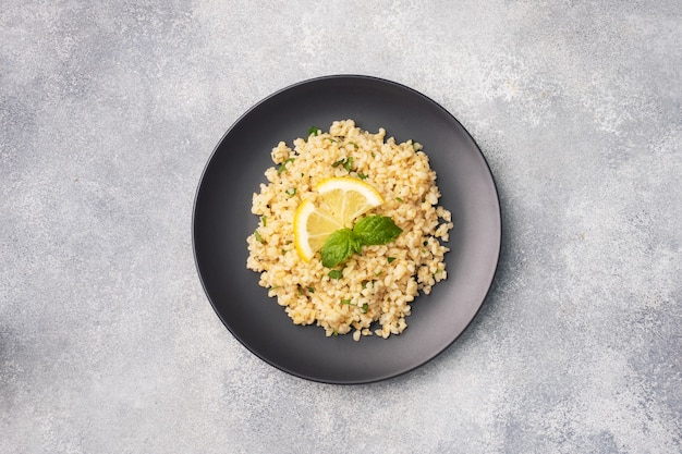 Gekochter bulgur mit frischer zitrone und minze auf einem teller. ein traditionelles orientalisches gericht namens tabouleh. draufsicht des grauen konkreten hintergrundes, kopienraum