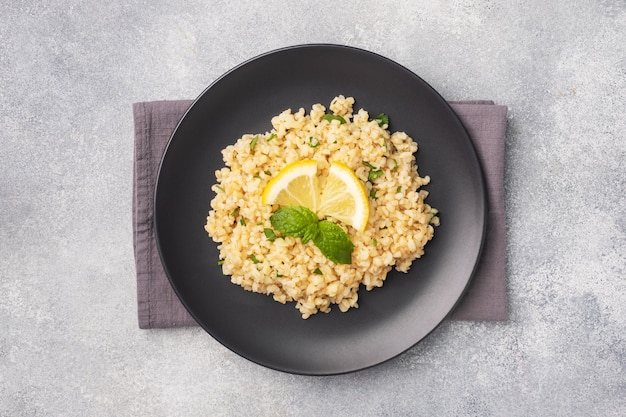 Gekochter Bulgur mit frischer Zitrone und Minze auf einem Teller. Ein traditionelles orientalisches Gericht namens Tabouleh. Draufsicht des grauen konkreten Hintergrundes, Kopienraum