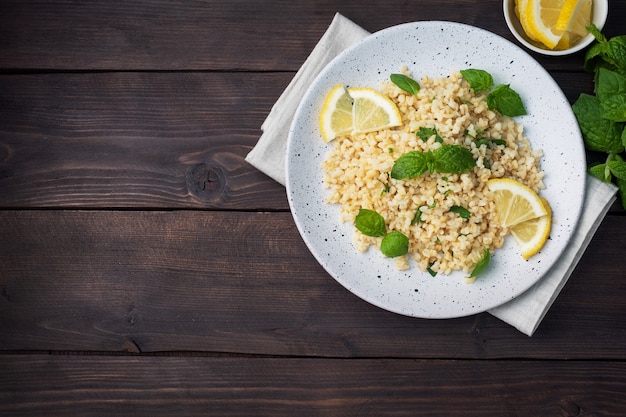 Gekochter Bulgur mit frischer Zitrone und Minze auf einem Teller. Ein traditionelles orientalisches Gericht namens Tabouleh. dunkler hölzerner Hintergrund. Ansicht von oben, Textfreiraum