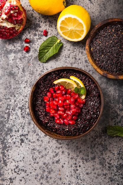 Gekochter thailändischer schwarzer Jasminreis mit Chiasamen, Granatapfel, Zitrone, Sesam auf grauem Betonhintergrund. Draufsicht