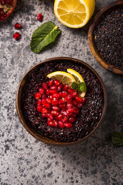 Gekochter thailändischer schwarzer Jasminreis mit Chiasamen, Granatapfel, Zitrone, Sesam auf grauem Betonhintergrund. Draufsicht