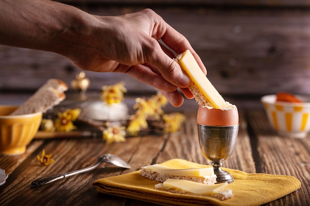 Gekochtes Ei in einem silbernen Eierbecher mit Brot und Käse auf einem Holztisch